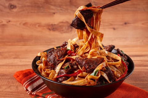 Udon noodles with beef in Mongolian style, with green onions and vegetables, served in a black