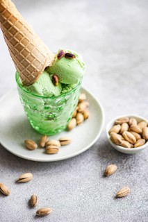 A close up of pistachio ice cream scoops in a green glass with a waffle cone, garnished with
