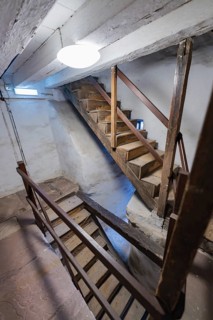 Old wooden staircase in a narrow, rustic stairwell with window and lighting, Prison Museum, Der