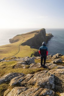 A walker looks up at Neistpoint Lighthouse in the morning light, Isle of skye, Great Britain