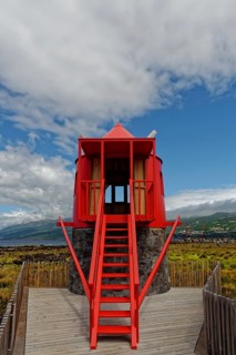 Red windmill Moinho das Lajes with a staircase leading up against a partly cloudy sky, fishing