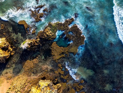 Aerial view of a rocky coastline with waves crashing against the shore, revealing stunning textures