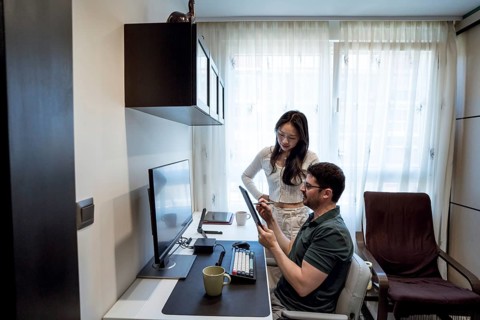 A diverse couple collaborates in a cozy home office, sharing ideas. The man sits at a desk, holding