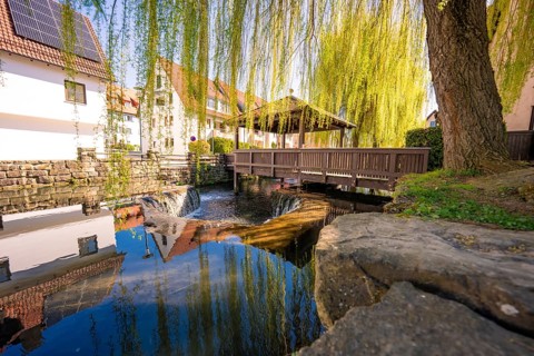 A wooden bridge with willows in the background is reflected in the water, Aidlingen, Böblingen