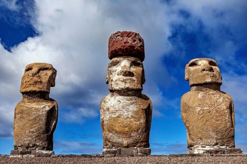 Close-up of three Moai statues, one with red stone headdress against a blue sky, The Moai Statues
