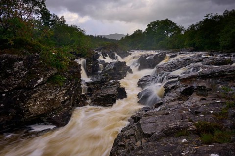 A torrential river in a rocky environment, nestled in nature and covered by a dark sky, River