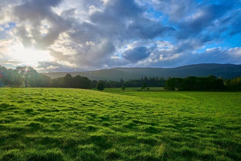 Green field under dramatic sky with sunset and mountains in the background, Fort Augustus, Loch