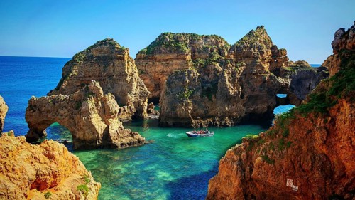 Natural wonder with rock arches and clear turquoise water, in which a boat with tourists, Ponta da