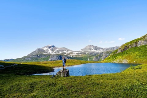 Hiker standing on a rock in front of a mountain landscape, small lake in the Flatvaddalen high