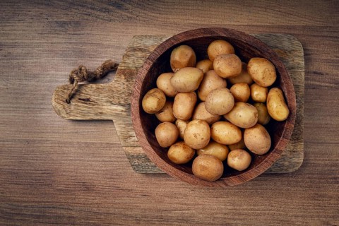 A rustic wooden bowl filled with freshly harvested small potatoes sits on a wooden cutting board,