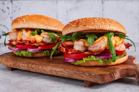 Two shrimp burgers and buns with sesame seeds, bacon, lettuce, tomatoes and onions, On a wooden