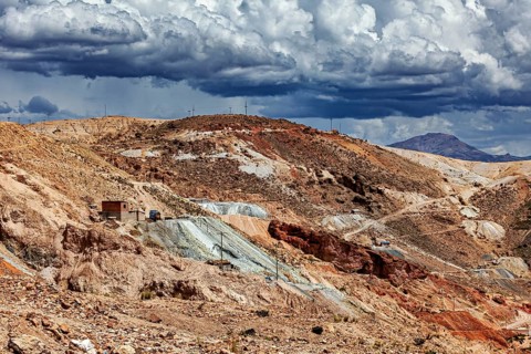 A dry hilly landscape with traces of mining activity under dramatic clouds, The silver mines near