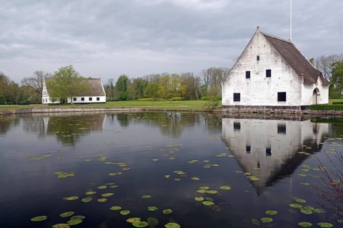 A white manor house on the banks of a pond, with clear reflections and floating water lilies,