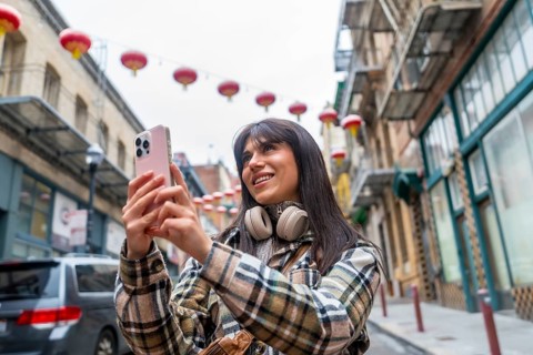 Young woman smiling and holding a smartphone, capturing content while exploring the vibrant street