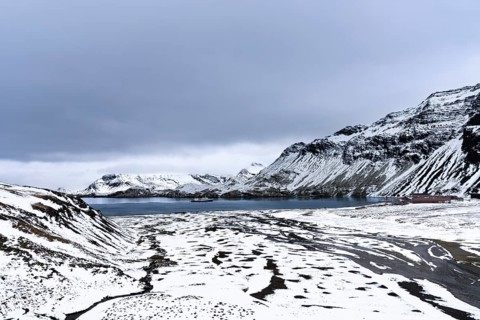 Snow-covered bay with expedition ship and former whaling station on the shore, surrounding