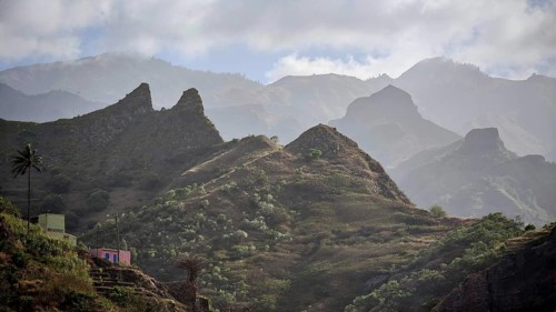 Hilly landscape with small houses and thick vegetation under cloudy skies, spectacular hiking,