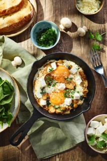 Fried eggs with spinach, mushrooms, grated cheese and feta cheese in small cast iron skillet. Top