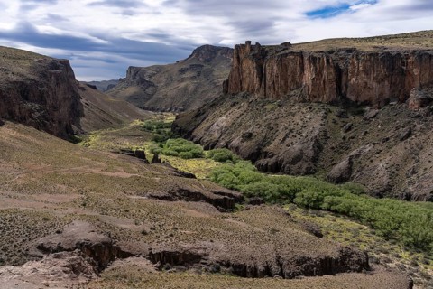 Río Pinturas canyon with steep rock walls and green valley floor, cloudy sky, Cueva de las Manos,