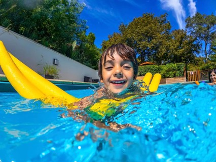 Small boy smiling and splashing in a bright blue swimming pool on a sunny summer day, enjoying