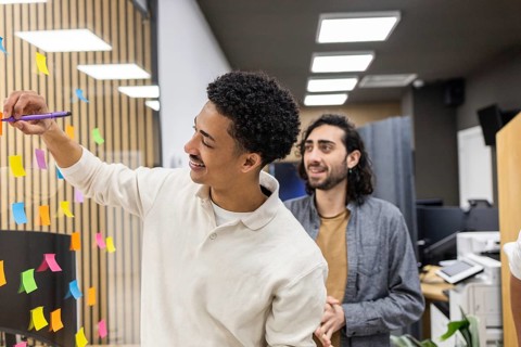Two young professionals engage in a creative brainstorming session at an office. One uses sticky