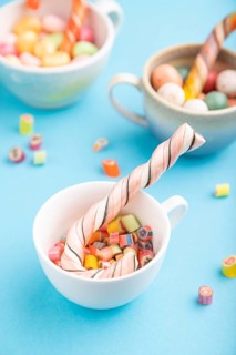 Heap of multicolored caramel candies in cups on blue pastel background. close up, side view,