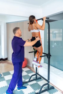 Young woman performing assisted pull ups using a resistance band on a workout station, guided by a