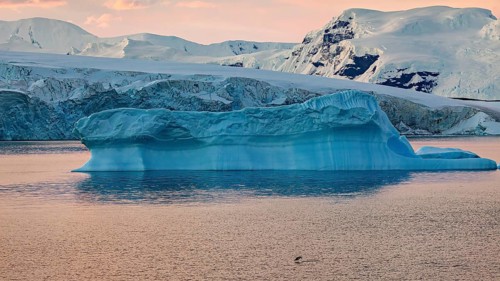 Large blue iceberg drifting in calm sea water at sunset, icebergs in the Southern Ocean in