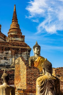 Stone Buddha statues, a high temple tower in the back, Prang, historic Buddhist temple complex,