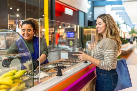 Friendly server preparing a custom dessert for a smiling customer selecting various toppings from a