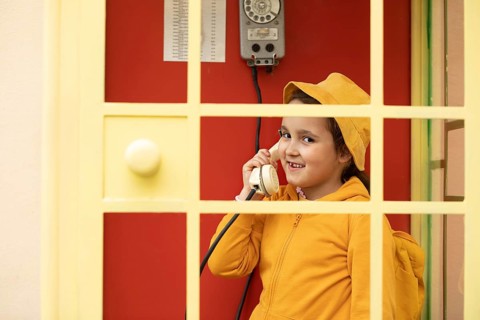 A young preteen girl smiles while talking on a retro style telephone. She is wearing a yellow hat