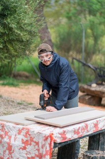 Man engages in woodworking outdoors, skillfully using a jigsaw to cut a board. He wears protective