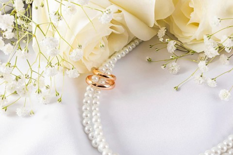Elegant wedding rings are showcased with delicate white flowers and pearls against a soft white
