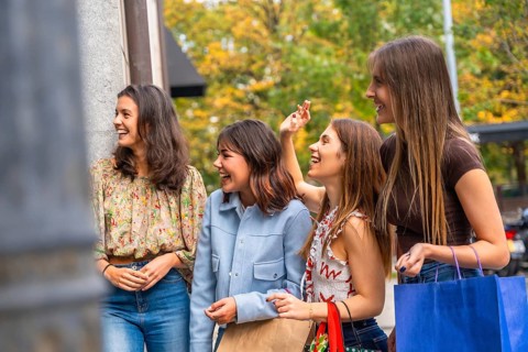 Four smiling young women, friends, walking outdoors, laughing and looking happily to the side while