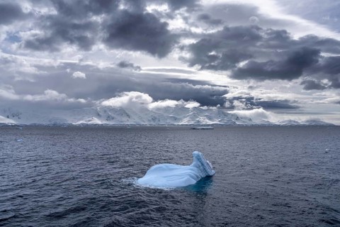 Small iceberg floating in the open water of the Southern Ocean with snow-capped mountains of the