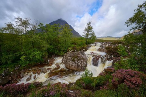 Fascinating landscape with waterfall in foreground and majestic mountain in background under cloudy
