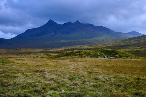 Rolling meadows in front of a massive mountain under dark clouds, Sligachan, Isle of Skye,