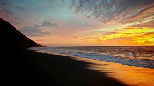 Glowing sunset on dark beach against mountains and glowing sky, volcanic sand, hiking, Tarrafal de