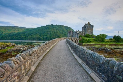 A rocky path leads to a historic castle surrounded by lush nature and rolling countryside, Eilean