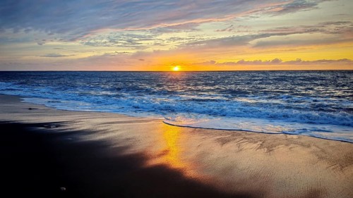A beautiful sunset over the sea reflects colors on a quiet sandy beach, volcanic sand, hiking,