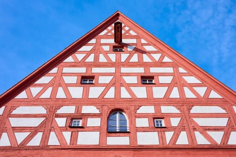 Detailed view of a timber-framed gable with symmetrical structures and windows against a blue sky,