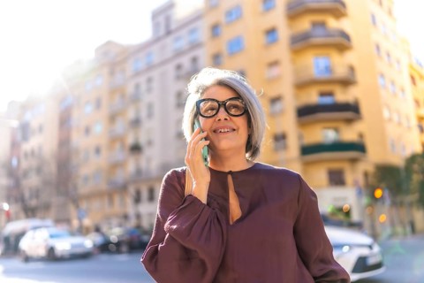 Smiling mature woman with glasses and gray hair talking on a mobile phone, representing modern
