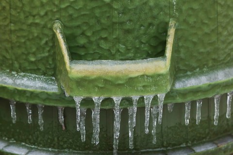 Handle on upside down green PVC and rubber thrash can covered with thick sheet of ice and hanging