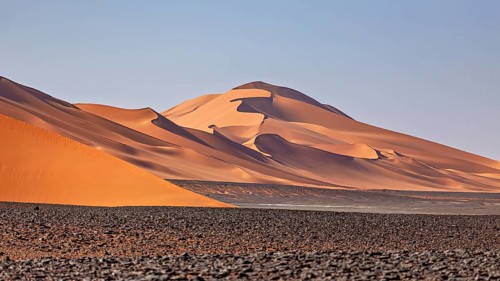 Gently curving sand dunes in an open desert landscape with a blue sky, The endless sand dunes of