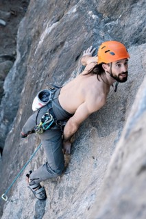 Person climbing in high mountain with rope without shirt and orange helmet in the wilderness.