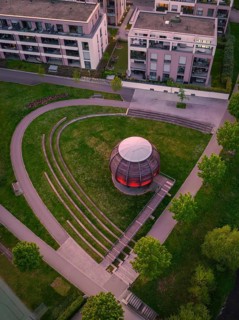 Aerial view of a modern wooden sphere on a green area, surrounded by buildings and symmetrical