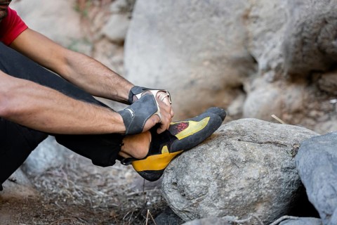 A climber prepares for a traditional climbing adventure in nature, adjusting their climbing shoe on
