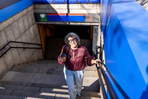 Senior woman commuters navigating subway stairs, holding a disposable coffee cup and backpack,