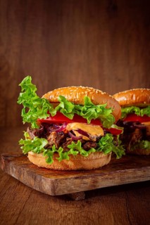Two burgers are stacked high with fresh lettuce, tomato slices, grilled onions, and a savory sauce.