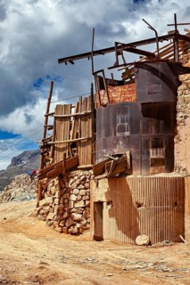 Dilapidated building made of wood and metal against a cloudy sky in a mountain landscape, The