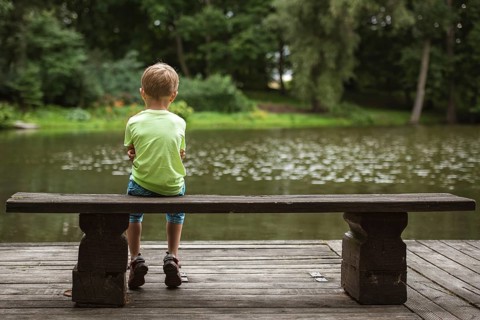 Small boy sit back on the wooden bench by the lake